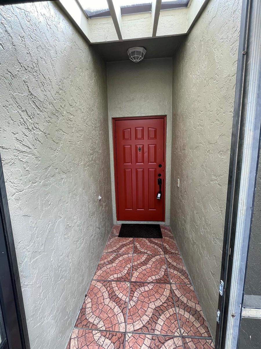 A red front door sits at the end of a narrow entryway with patterned tile flooring — 172 Meadows Drive, Boynton Beach FL 33436, BOYNTON BEACH, FL