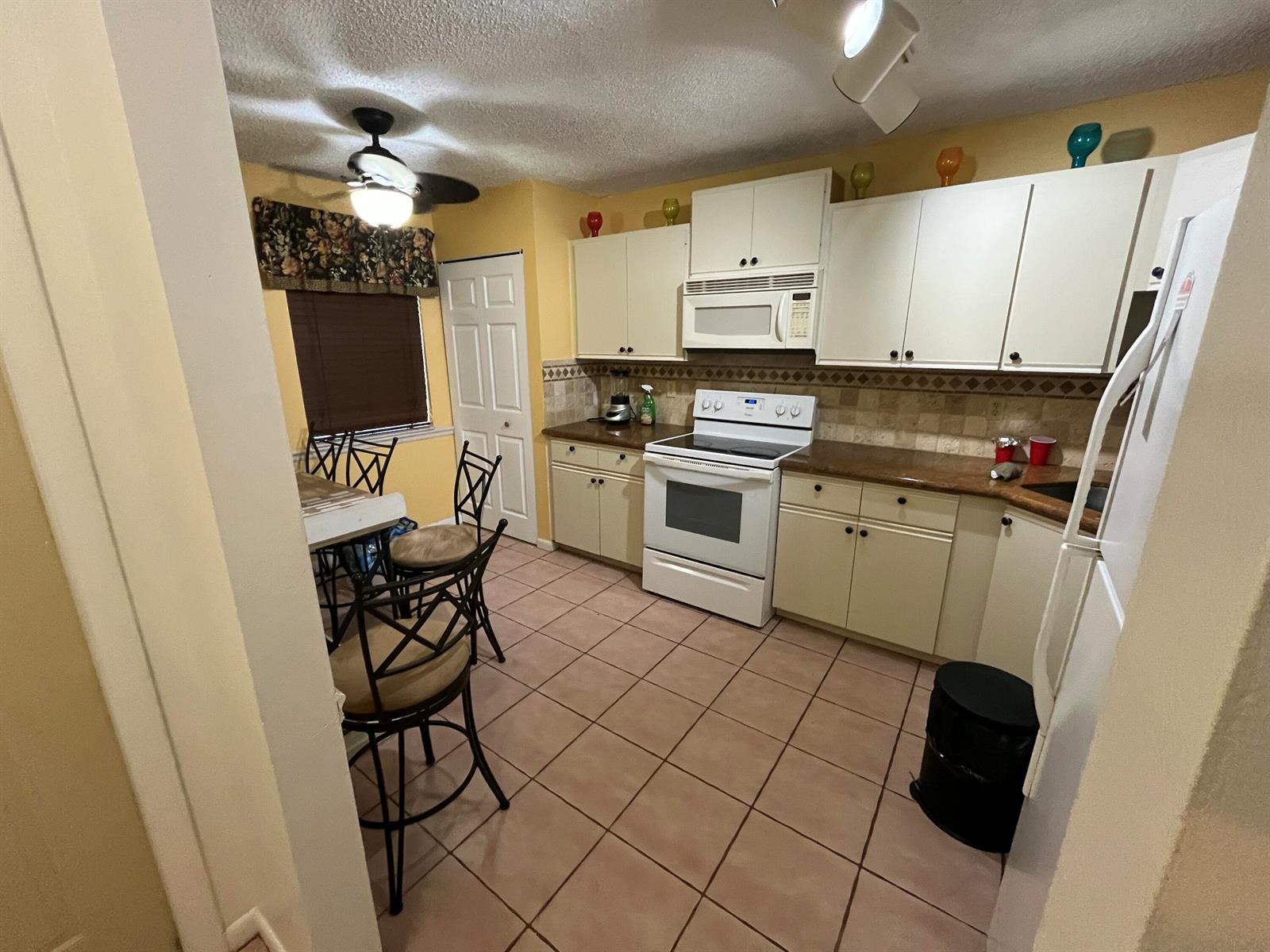 A kitchen features off-white cabinets, a white stove, tile flooring, and a small dining area — 172 Meadows Drive, Boynton Beach FL 33436, BOYNTON BEACH, FL