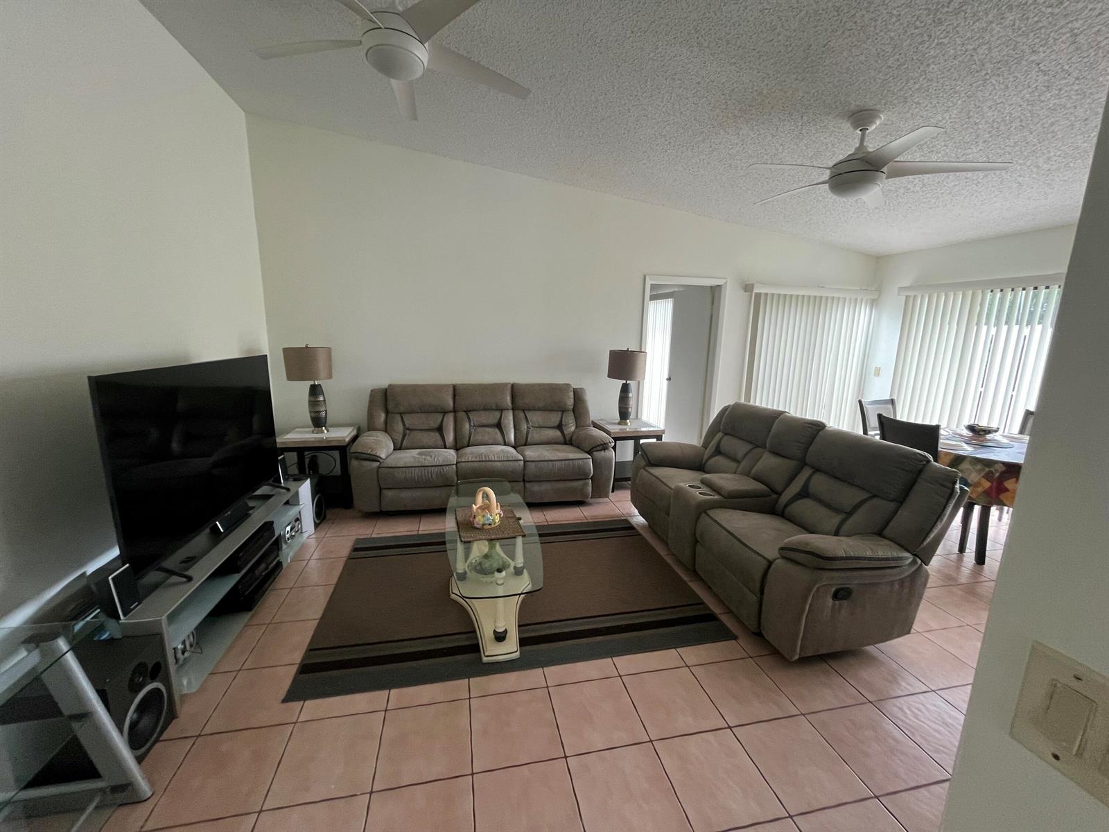 A living room features two brown reclining sofas, a glass coffee table, and tile flooring — 172 Meadows Drive, Boynton Beach FL 33436, BOYNTON BEACH, FL