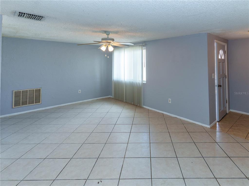 An empty room features light blue walls, beige tile flooring, and a ceiling fan — 4150 NEWBURY DRIVE, NEW PORT RICHEY, FL