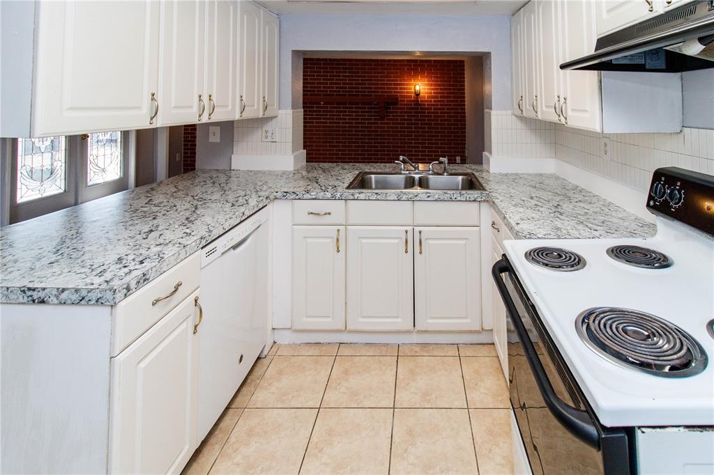 A kitchen features white cabinets, granite countertops, a double sink, and a brick accent wall — 4150 NEWBURY DRIVE, NEW PORT RICHEY, FL