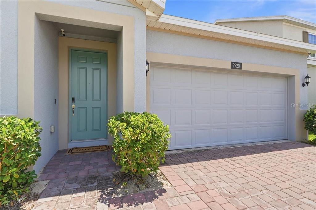 A light blue front door and a white garage door face a brick paver driveway — 2720 NOTTEL DRIVE, ST CLOUD, FL