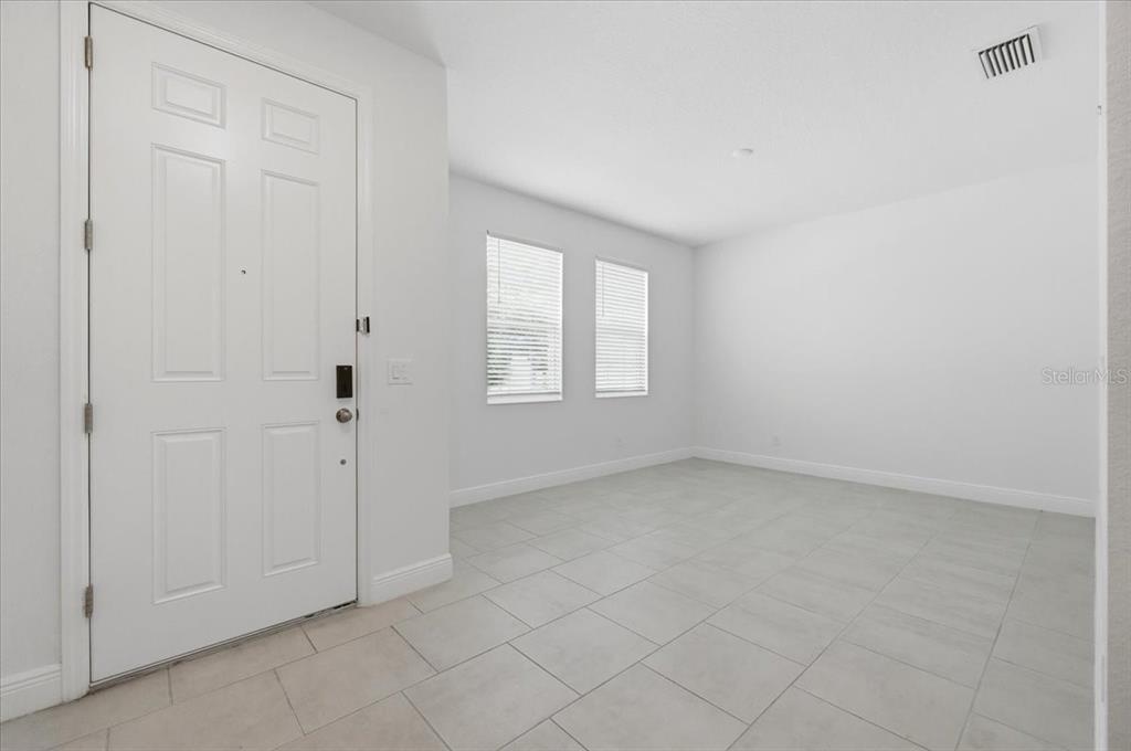 An empty room with white walls, light tile flooring, two windows, and a white door — 2720 NOTTEL DRIVE, ST CLOUD, FL