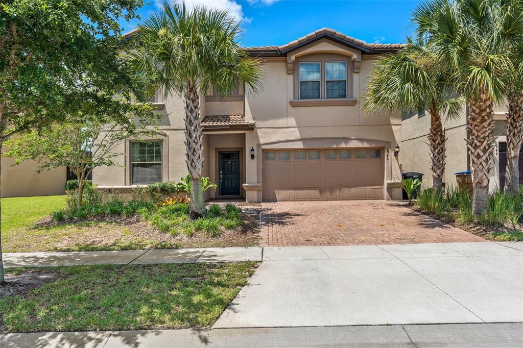 A two-story tan stucco house features a brick driveway, a two-car garage, and palm trees — 1940 NICE COURT, KISSIMMEE, FL