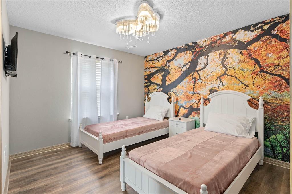A bedroom features two twin beds, a large autumn-themed wall mural, and a crystal chandelier — 1940 NICE COURT, KISSIMMEE, FL