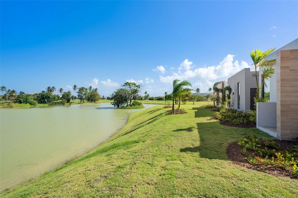 A modern house exterior overlooks a grassy lawn and a pond under a clear sky — 15 THE ISLES AT DORADO BEACH, DORADO, PR