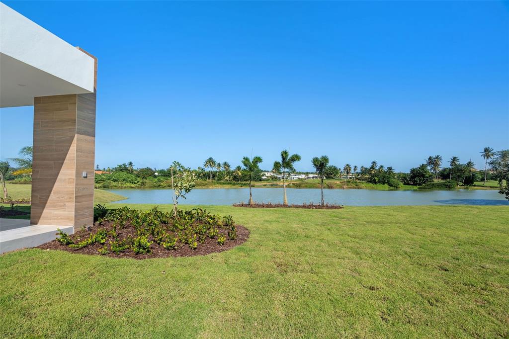 A modern home exterior overlooks a grassy lawn, a small pond, and distant palm trees — 15 THE ISLES AT DORADO BEACH, DORADO, PR