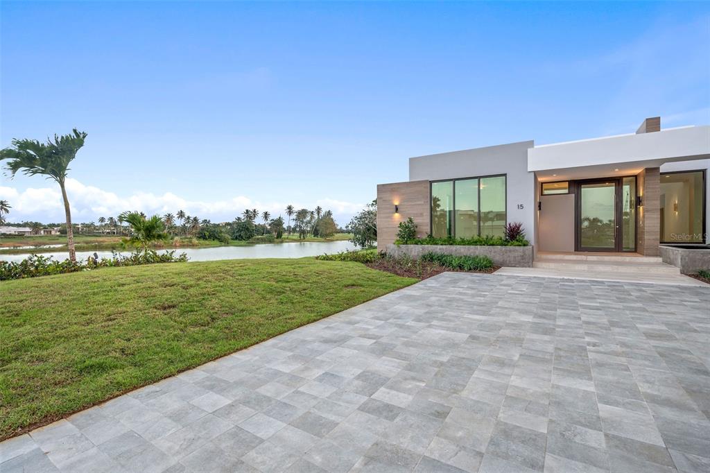 A modern house with a paved driveway, large windows, and a view of a lake — 15 THE ISLES AT DORADO BEACH, DORADO, PR