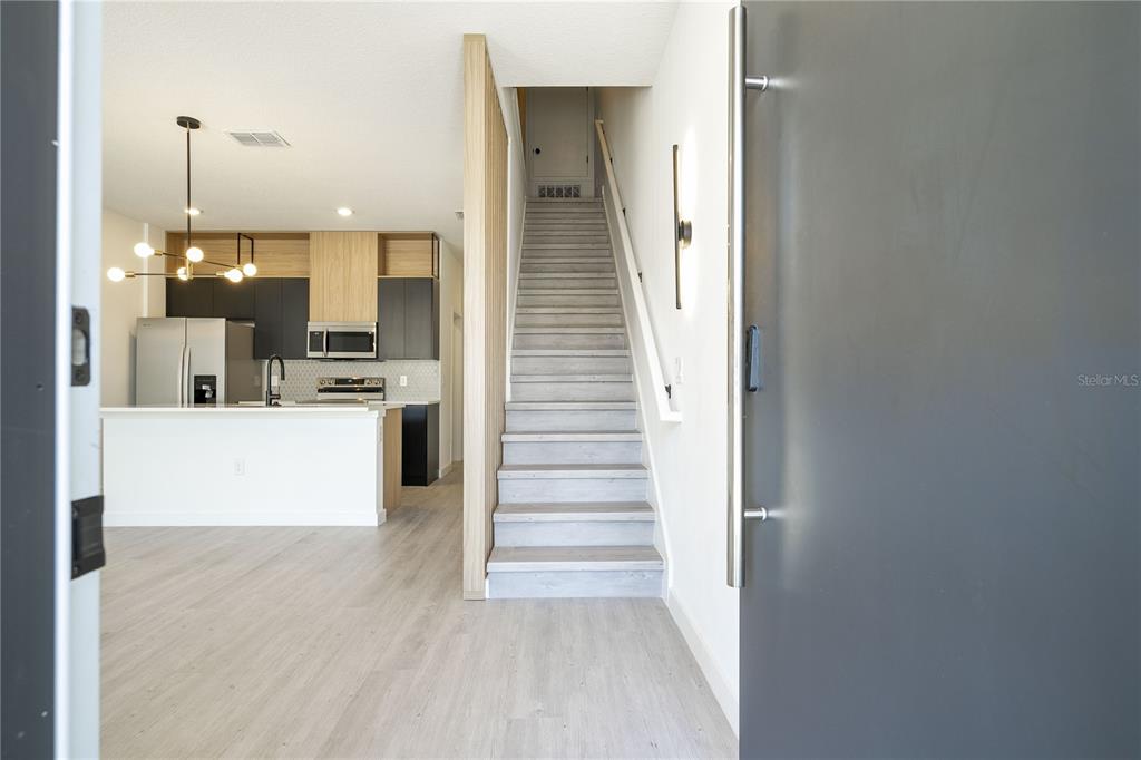 A view from an entryway showing a staircase, light wood flooring, and a modern kitchen — 3245 TRANQUIL TRAIL, KISSIMMEE, FL