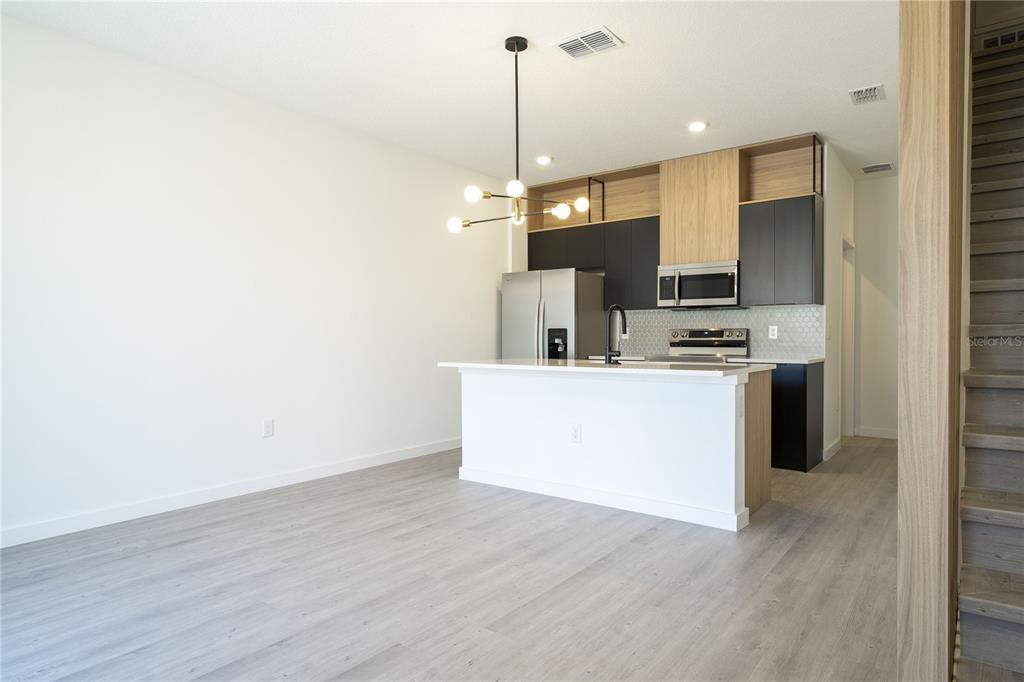 A modern kitchen features black and wood-tone cabinetry, a white island, and light wood flooring — 3245 TRANQUIL TRAIL, KISSIMMEE, FL