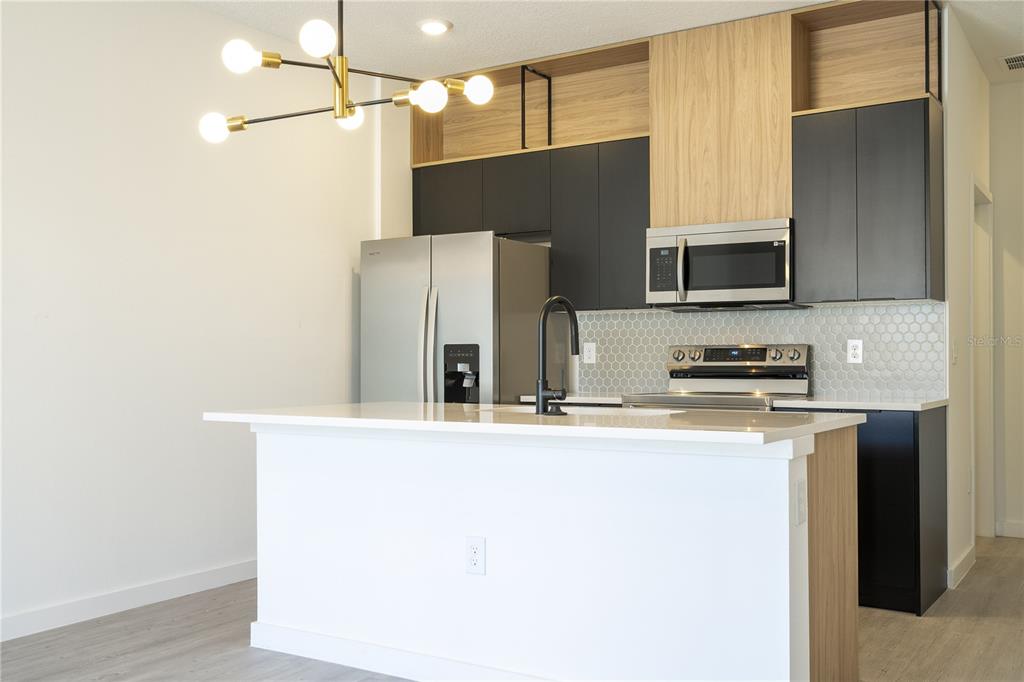 A modern kitchen features a white island, dark cabinetry, light wood accents, and stainless appliances — 3245 TRANQUIL TRAIL, KISSIMMEE, FL