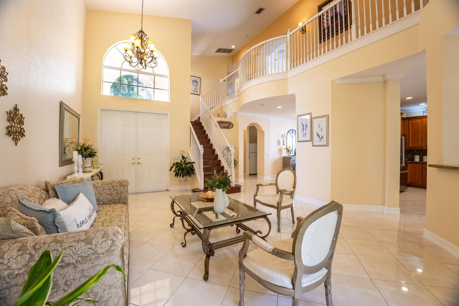 A bright, two-story foyer features a grand staircase, tile flooring, and a formal seating area — 8789 Sandy Crest Lane, Boynton Beach FL 33473, BOYNTON BEACH, FL