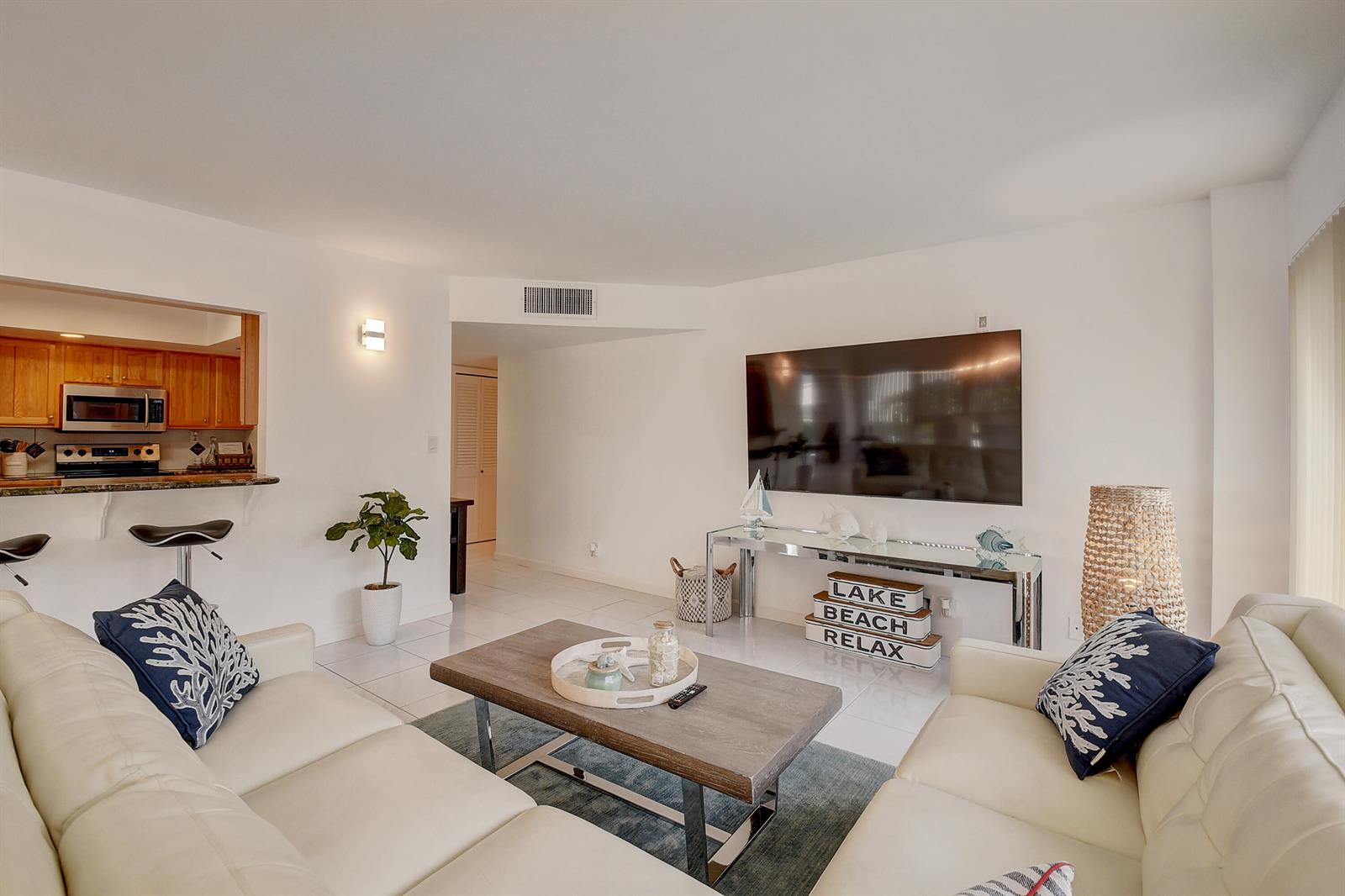 A living room with white sofas, a coffee table, and a wall-mounted television — 2066 N Ocean Boulevard, Boca Raton FL 33431, BOCA RATON, FL