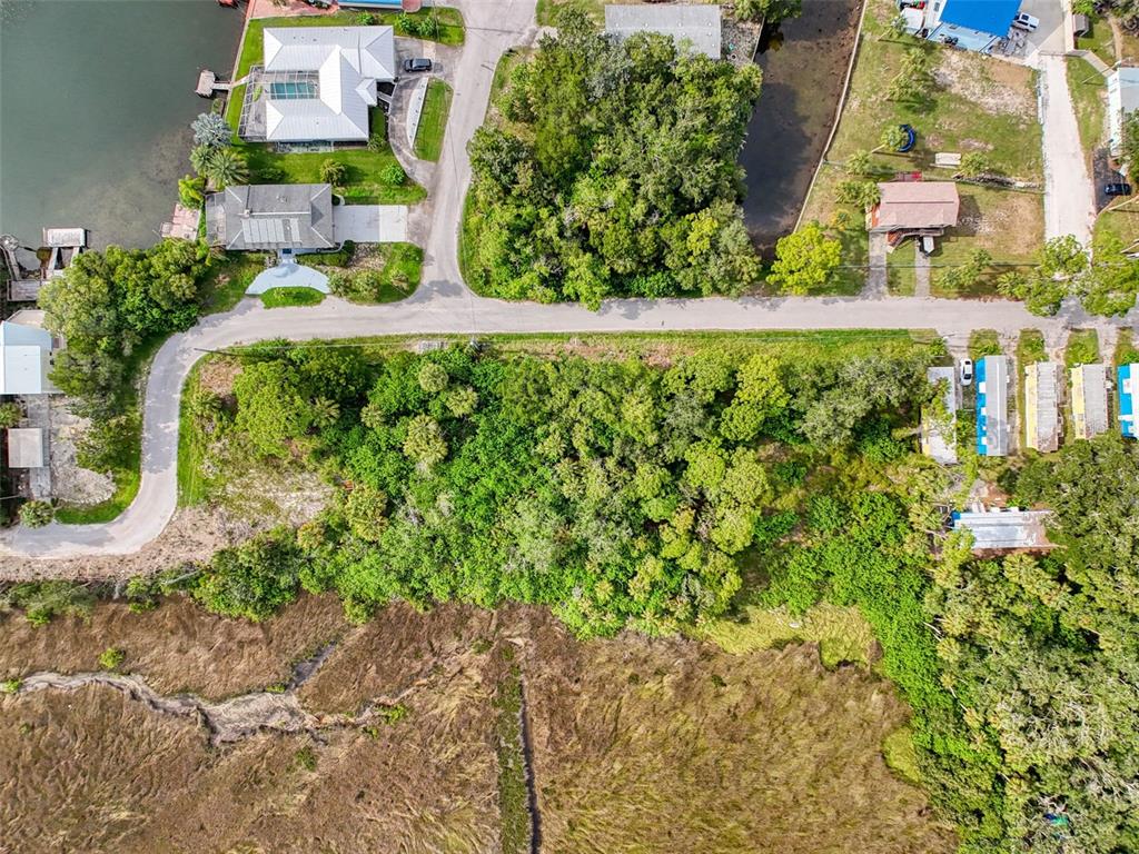 An aerial view shows a wooded lot bordered by a road, marshland, and nearby houses — LOT 8 NOWIKI AVENUE, HUDSON, FL