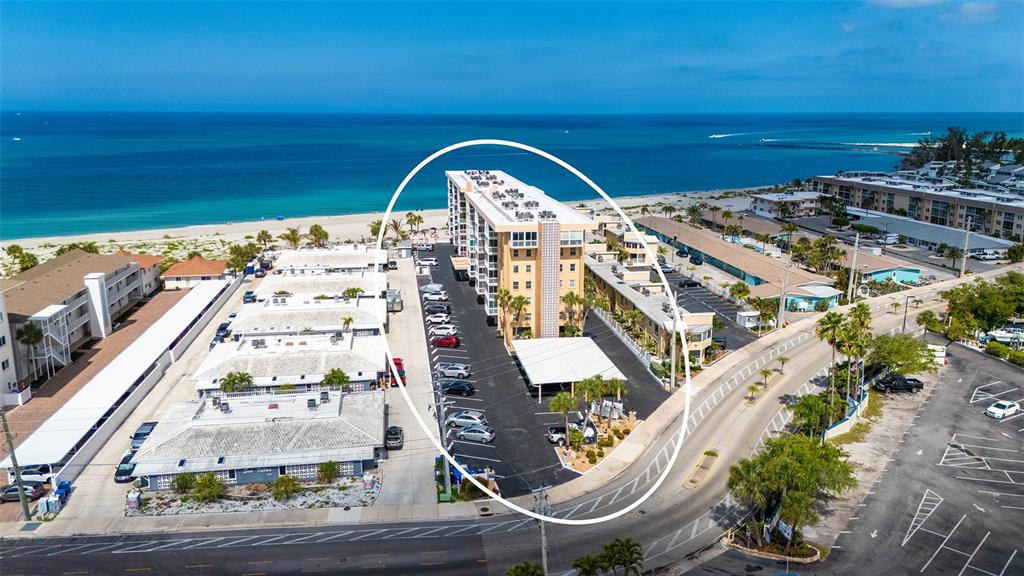 An aerial view shows a multi-story apartment building with a parking lot near the beach — 1255 TARPON CENTER DRIVE UNIT 406, VENICE, FL