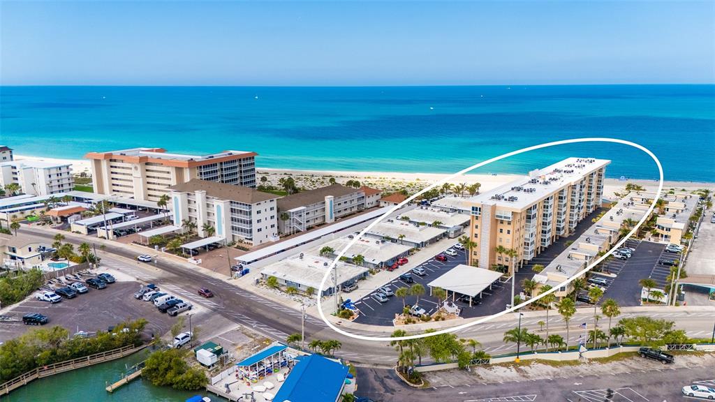 An aerial view shows a multi-story beachfront apartment building with a parking lot — 1255 TARPON CENTER DRIVE UNIT 406, VENICE, FL