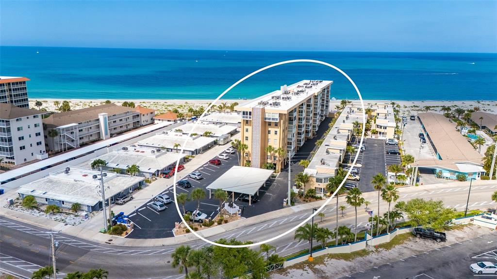 An aerial view shows a multi-story apartment building surrounded by a parking lot and beach — 1255 TARPON CENTER DRIVE UNIT 406, VENICE, FL