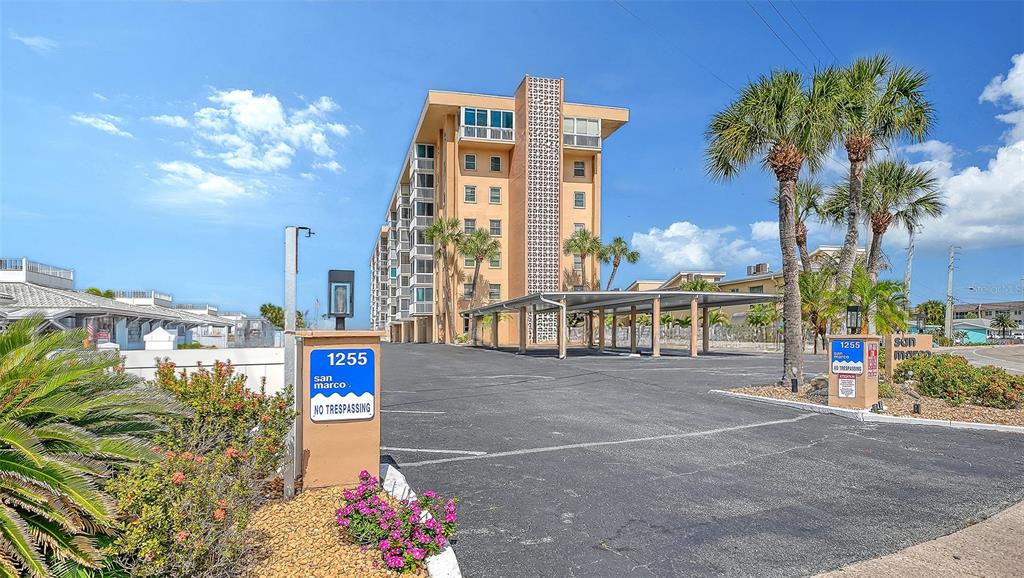 An exterior view of a multi-story apartment building with a covered parking area and palm trees — 1255 TARPON CENTER DRIVE UNIT 406, VENICE, FL