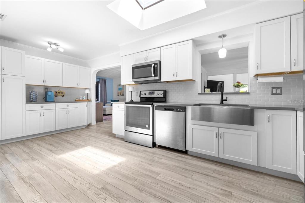 A kitchen with white cabinets, stainless steel appliances, a farmhouse sink, and light wood flooring — 144 BEVERLY DR, WINTER HAVEN, FL