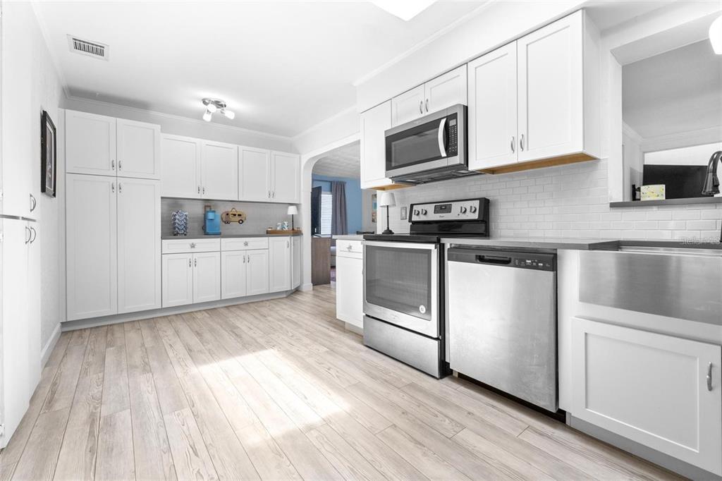 A modern kitchen features white cabinetry, stainless steel appliances, a farmhouse sink, and light flooring — 144 BEVERLY DR, WINTER HAVEN, FL