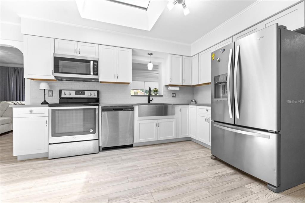 A kitchen features white cabinets, stainless steel appliances, a farmhouse sink, and light wood flooring — 144 BEVERLY DR, WINTER HAVEN, FL
