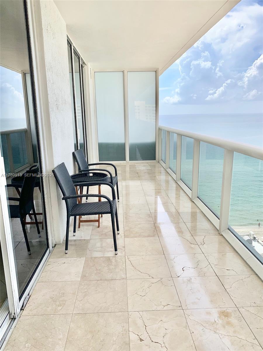 A balcony with tiled flooring, two chairs, and a glass railing overlooking the ocean — 1830 S Ocean Dr # 1503, Hallandale Beach FL 33009, HALLANDALE BEACH, FL
