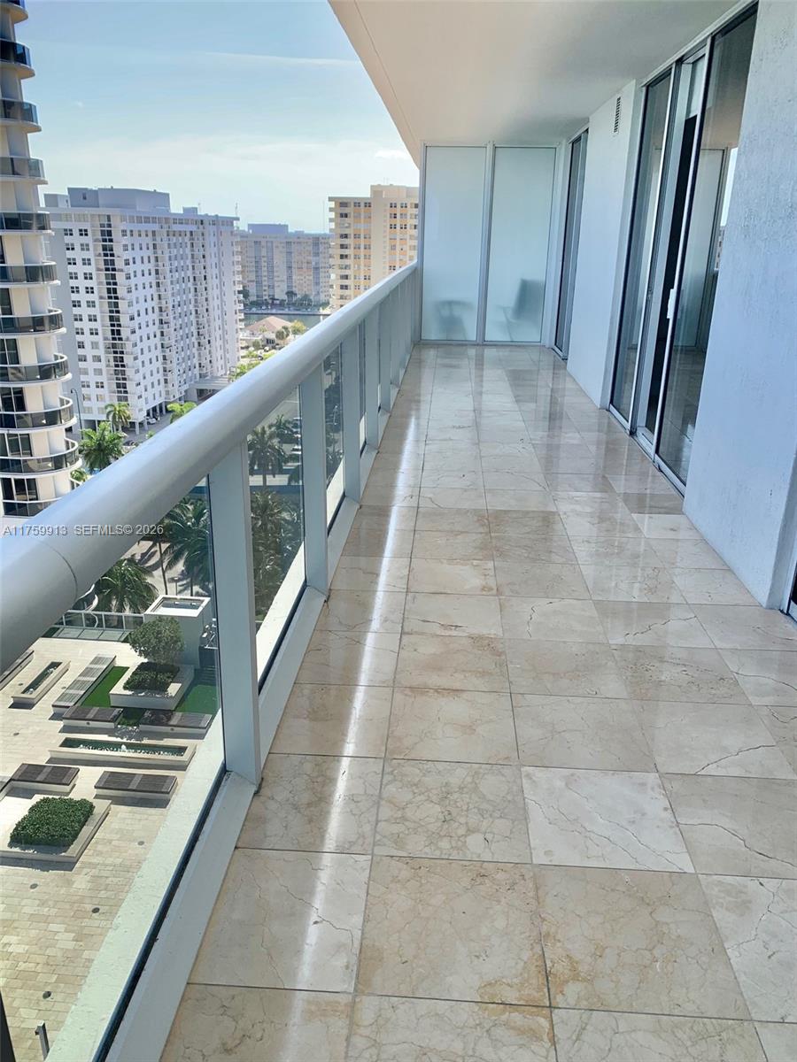 A high-rise balcony features light-colored stone tile flooring and a glass railing overlooking city buildings — 1830 S Ocean Dr # 1503, Hallandale Beach FL 33009, HALLANDALE BEACH, FL