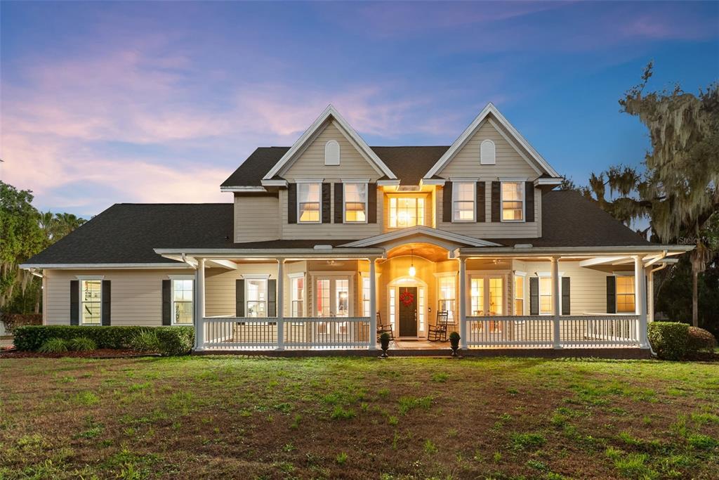 A two-story house with beige siding, a large front porch, and two gabled roof dormers — 10913 BRIGANN YARD WAY, THONOTOSASSA, FL