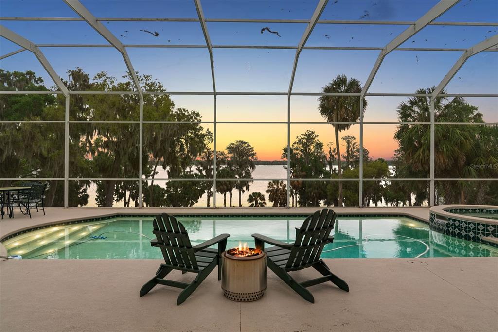 A screened-in pool patio features two chairs, a fire pit, and a lake view — 10913 BRIGANN YARD WAY, THONOTOSASSA, FL