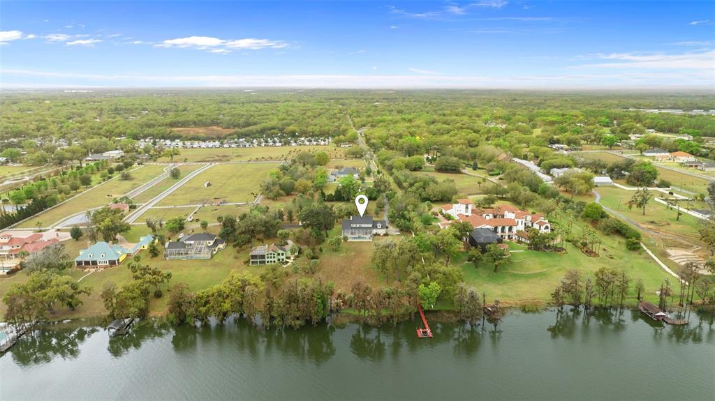An aerial view shows a house with a location pin situated on a grassy lakeshore — 10913 BRIGANN YARD WAY, THONOTOSASSA, FL