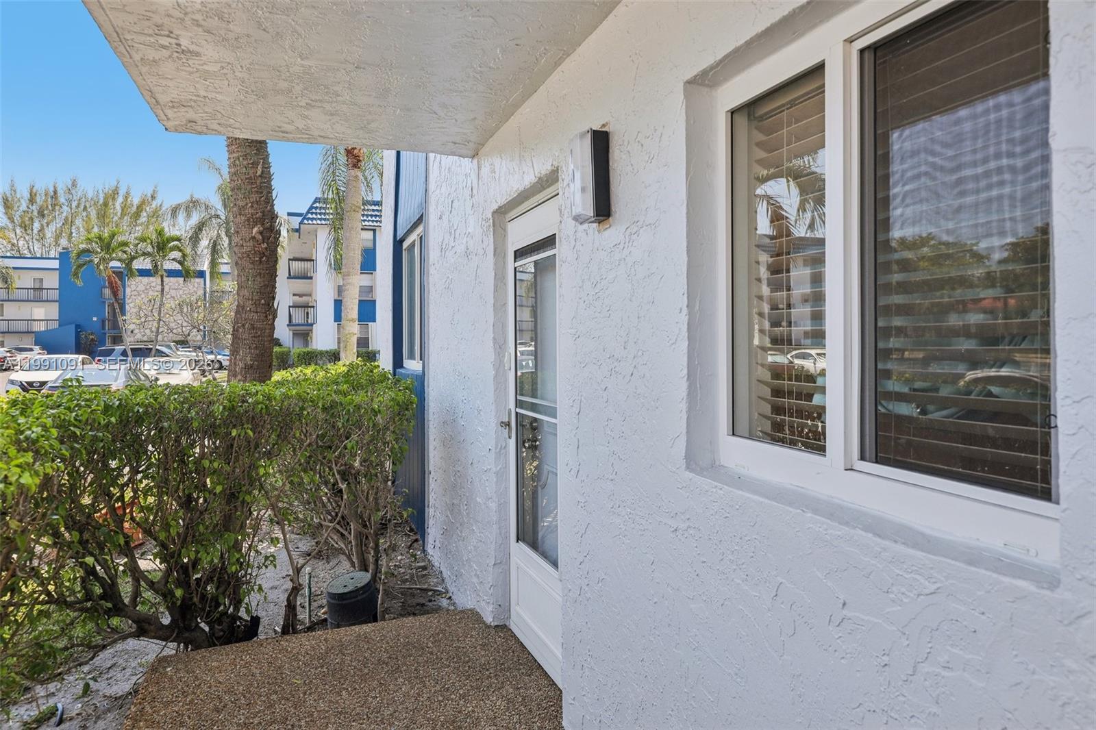 A white stucco exterior wall features a glass storm door and a window with blinds — 3050 N Holiday Springs Blvd # 101, Margate FL 33063, MARGATE, FL