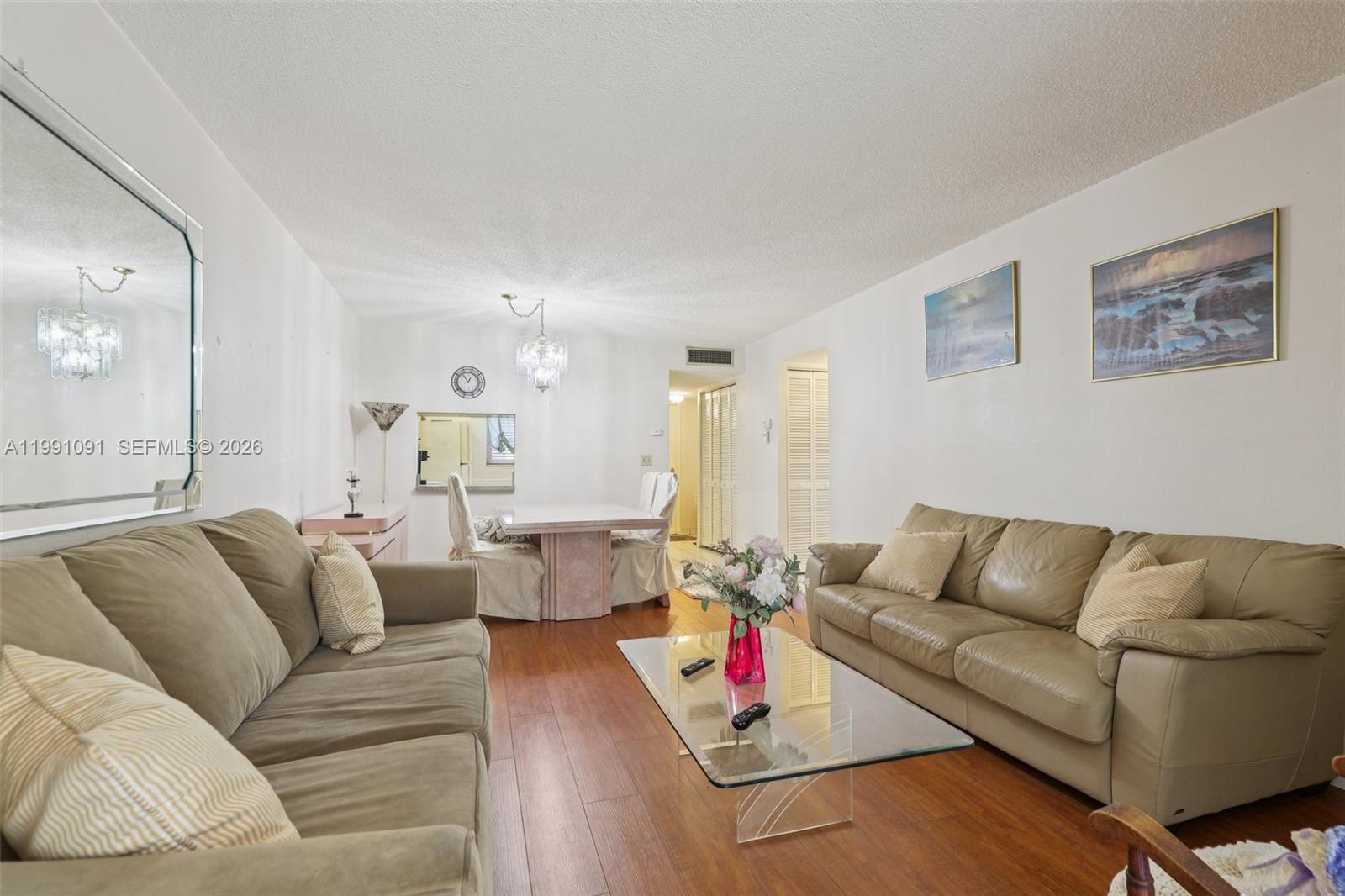 A living room with wood flooring, two beige sofas, and a glass coffee table — 3050 N Holiday Springs Blvd # 101, Margate FL 33063, MARGATE, FL
