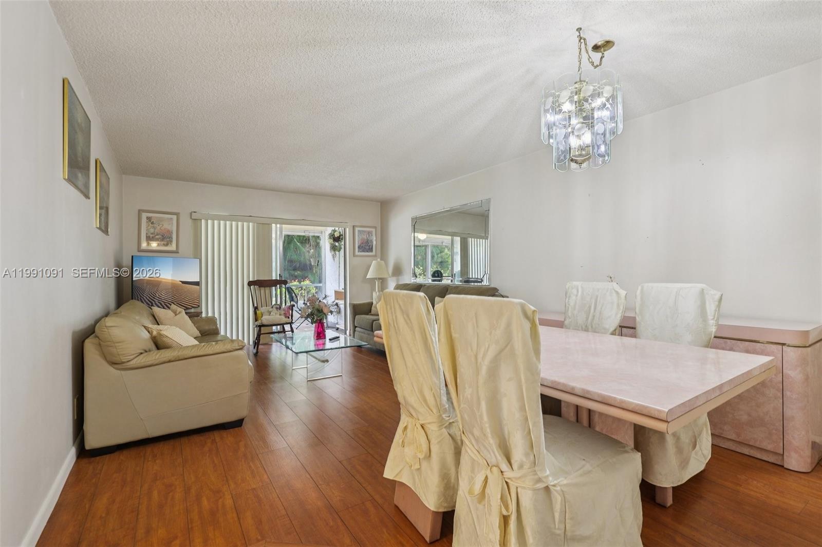A living and dining room features wood-look flooring, a glass chandelier, and neutral furniture — 3050 N Holiday Springs Blvd # 101, Margate FL 33063, MARGATE, FL