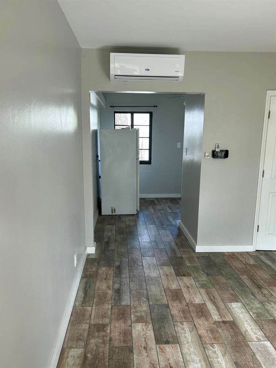 A room with wood-look tile flooring leads to a kitchen area featuring a white refrigerator — 214 S Palmway, FL 33460, FL