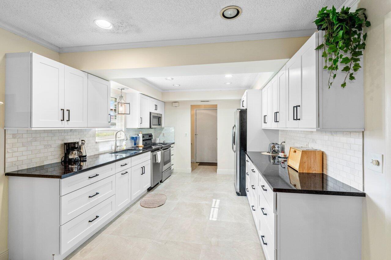 A galley kitchen features white cabinets, black countertops, stainless steel appliances, and light tile flooring — 4265 Shelldrake Lane, Boynton Beach FL 33436, BOYNTON BEACH, FL