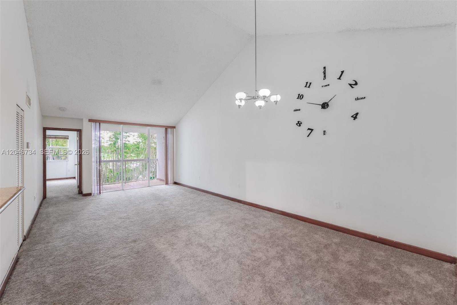 An empty living room features a vaulted ceiling, beige carpeting, and a large wall clock — 4990 NW 97th Pl # 314, Doral FL 33178, DORAL, FL