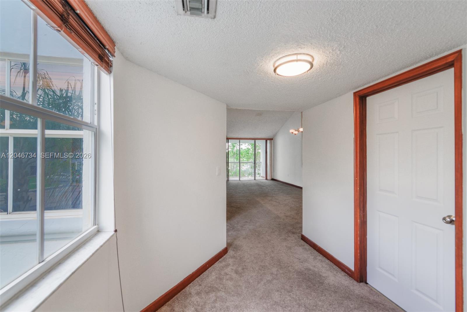 A carpeted hallway leads to a living area with a balcony and large windows — 4990 NW 97th Pl # 314, Doral FL 33178, DORAL, FL