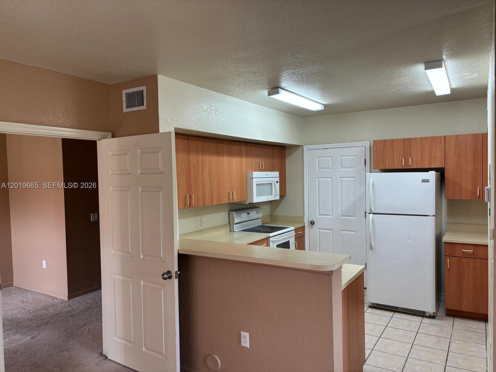 A kitchen features wood-tone cabinets, white appliances, a breakfast bar, and tile flooring — NORTH LAUDERDALE, FL