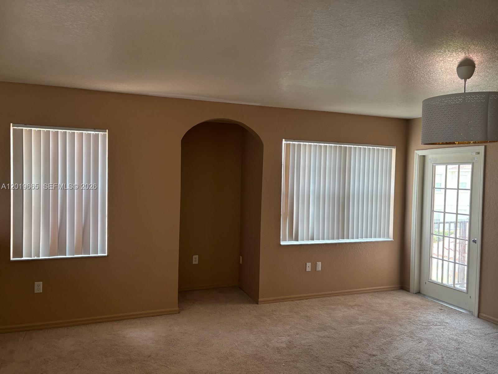 A carpeted room features tan walls, two windows with vertical blinds, and an arched alcove — NORTH LAUDERDALE, FL