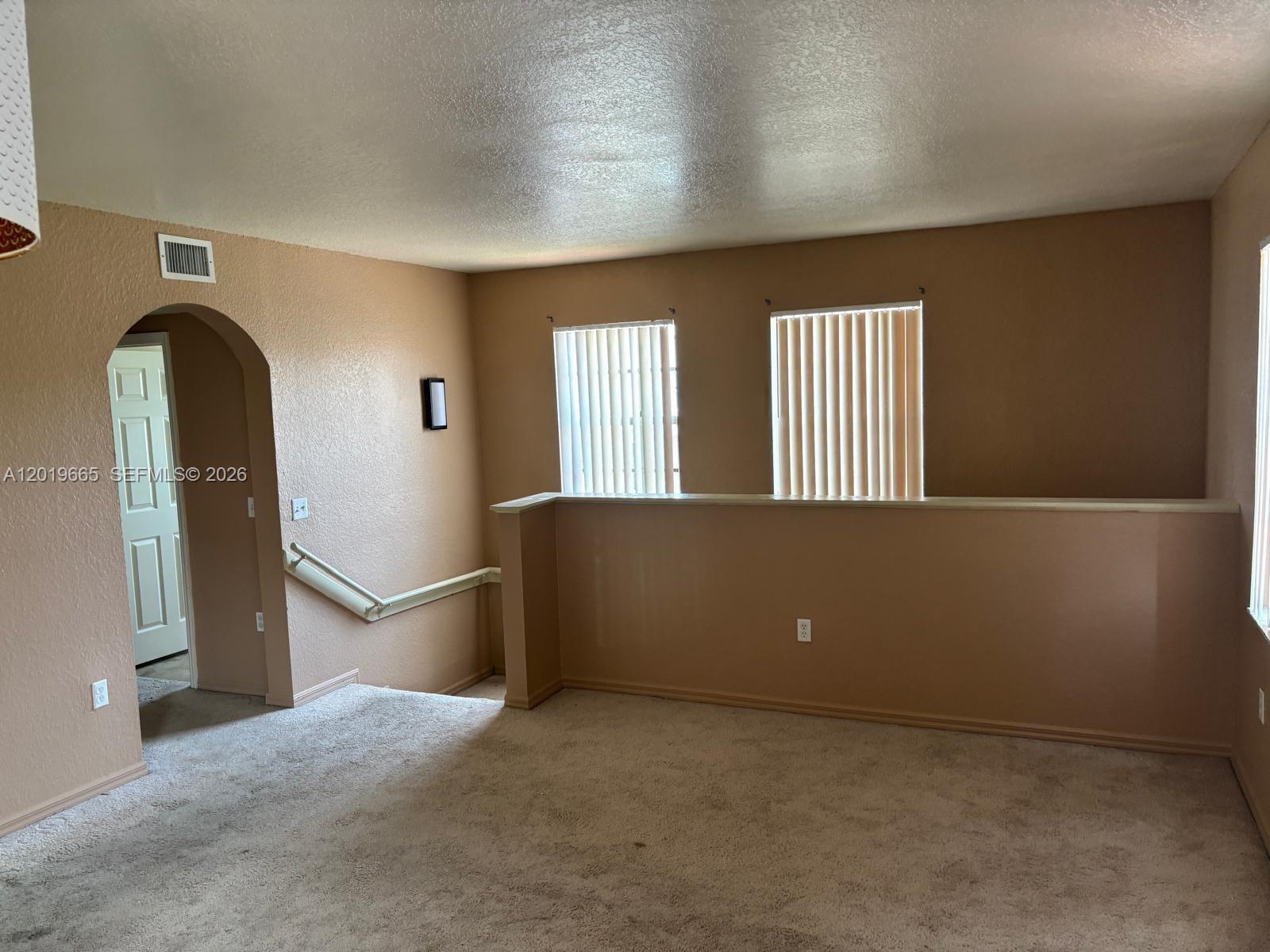 A carpeted room features an arched doorway, a half-wall, and two windows with vertical blinds — NORTH LAUDERDALE, FL