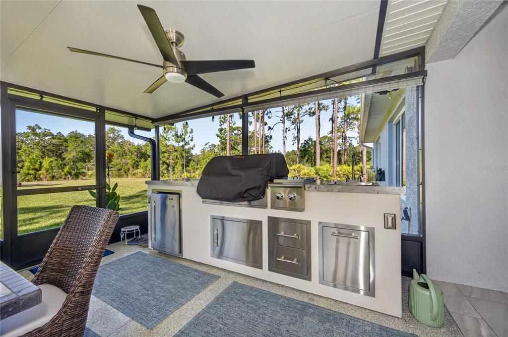 A covered outdoor kitchen features stainless steel appliances, a grill, and a view of trees — 4101 POINCIANA DRIVE, INDIAN LAKE ESTATES, FL