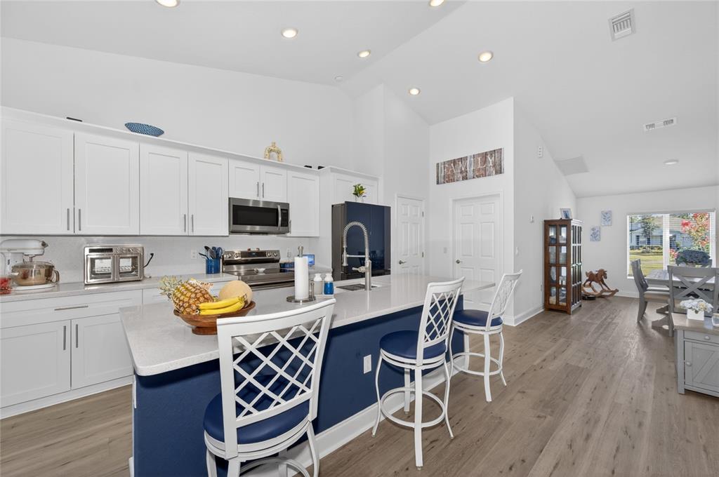A kitchen features white cabinets, a blue island with bar seating, and light wood flooring — 4101 POINCIANA DRIVE, INDIAN LAKE ESTATES, FL