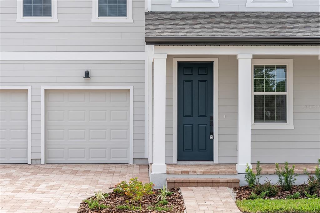 A gray house exterior features a dark blue front door, a garage, and a paved walkway — 12890 EUREKA LEMON DRIVE, WINTER GARDEN, FL