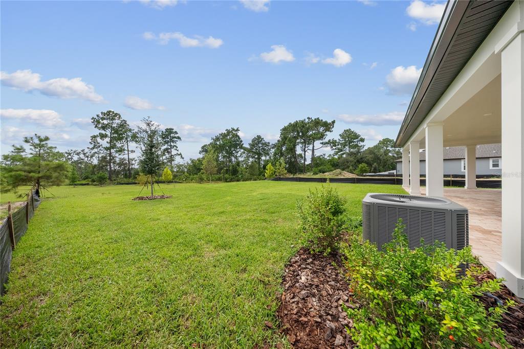 A backyard view showing a covered patio, an air conditioning unit, and a grassy lawn — 12890 EUREKA LEMON DRIVE, WINTER GARDEN, FL