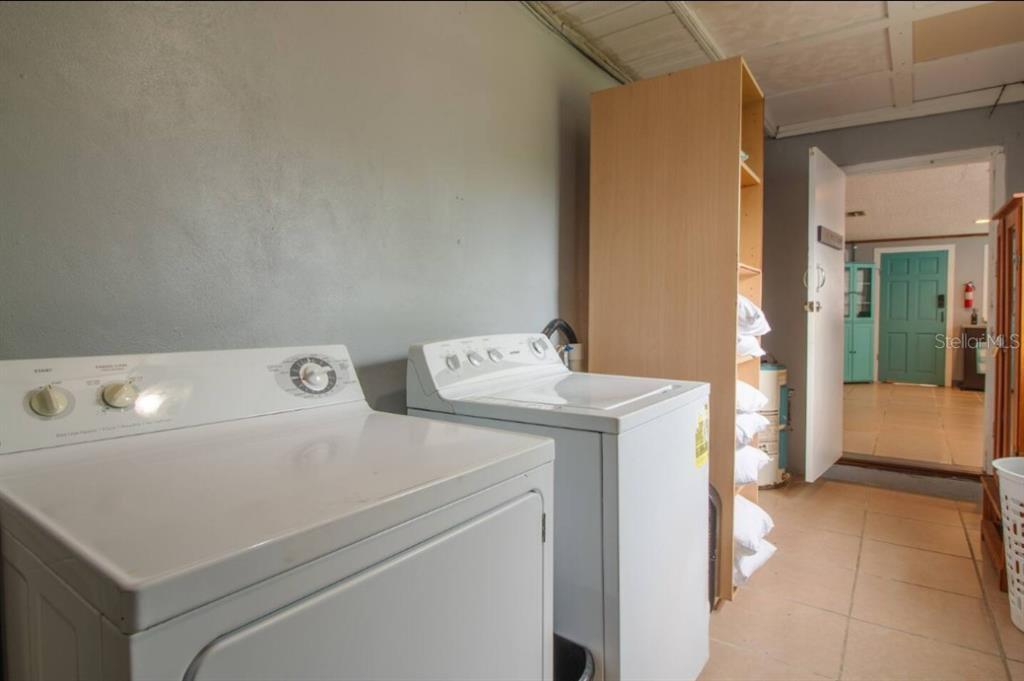 A laundry room features a white washer and dryer next to a tall wooden shelving unit — 1731 GRAYSON DRIVE UNIT 2, ORLANDO, FL