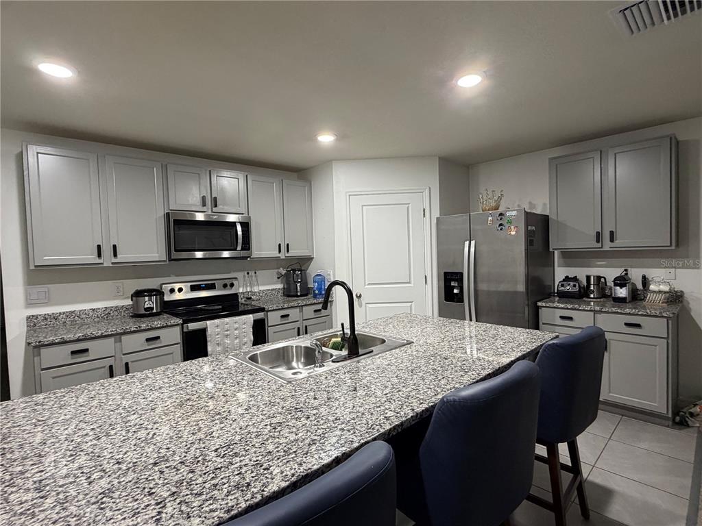 A kitchen features gray cabinets, granite countertops, stainless steel appliances, and a central island — 17425 NW 173 ROAD, ALACHUA, FL