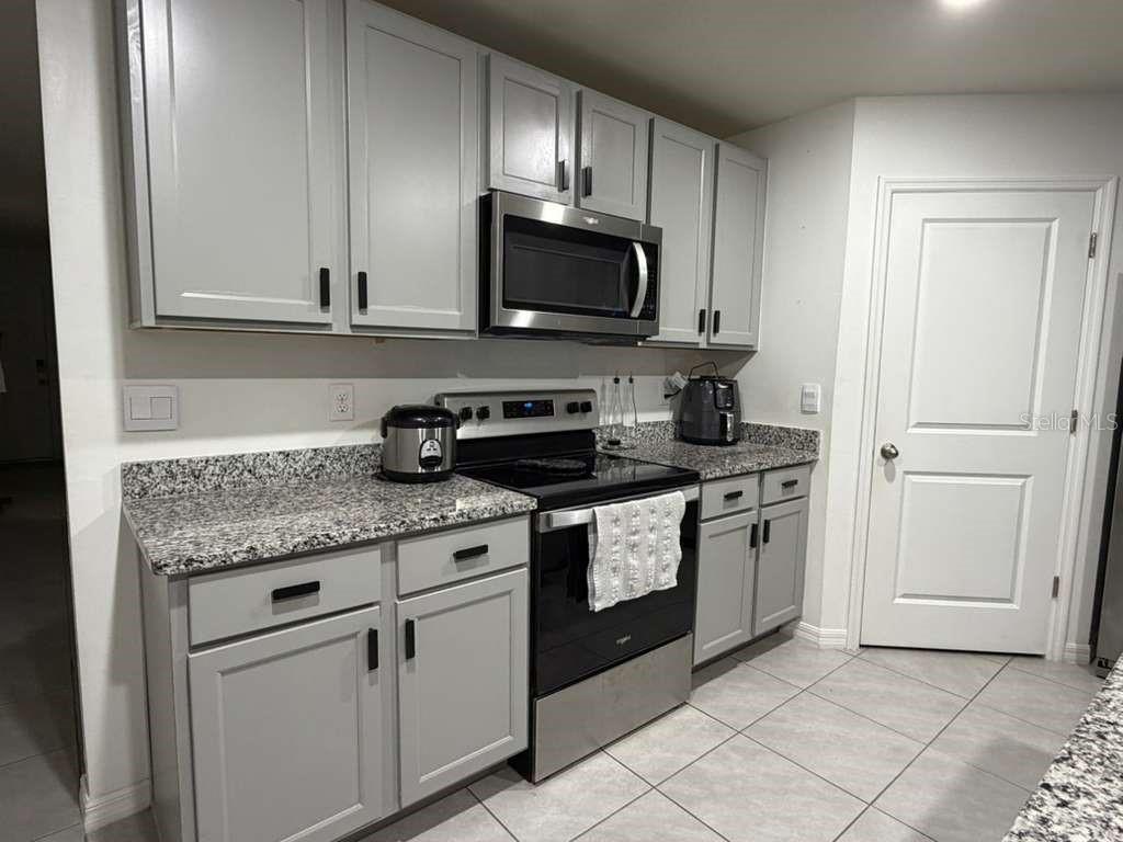 A kitchen features gray cabinets, granite countertops, stainless steel appliances, and light-colored tile flooring — 17425 NW 173 ROAD, ALACHUA, FL
