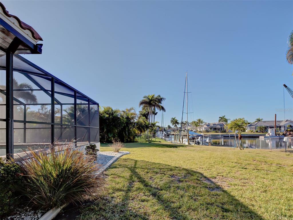 A view of a grassy backyard with a pool enclosure overlooking a canal with boats — 2301 VIA VENETO DRIVE, PUNTA GORDA, FL