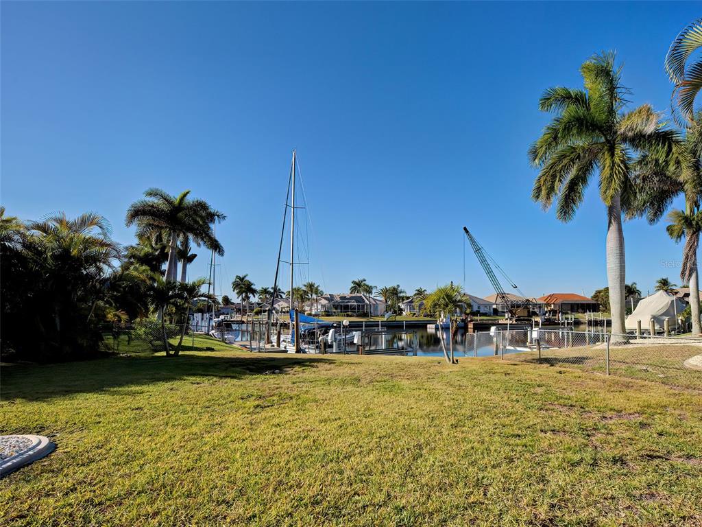 A grassy backyard overlooks a canal with boat docks, palm trees, and a construction crane — 2301 VIA VENETO DRIVE, PUNTA GORDA, FL