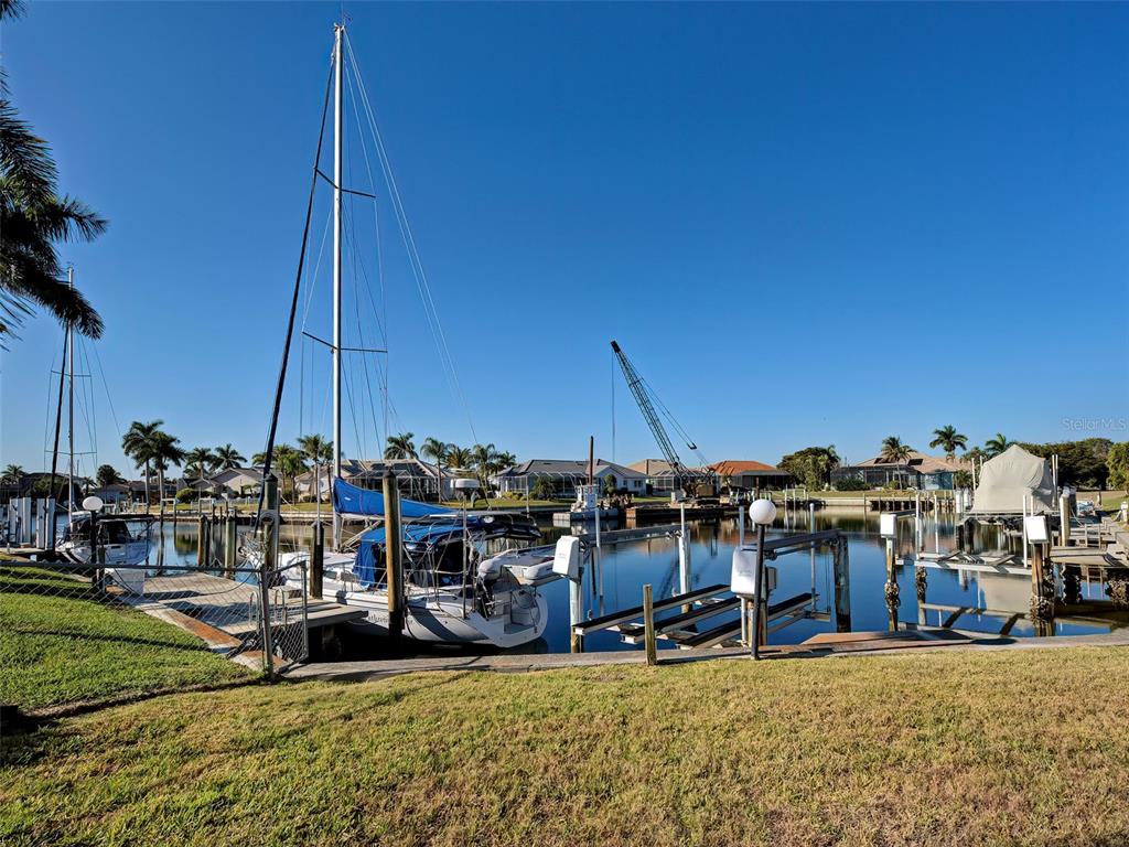 A sailboat is docked at a canal behind residential homes under a clear blue sky — 2301 VIA VENETO DRIVE, PUNTA GORDA, FL